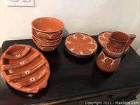 Terracotta tableware set including bowls, plates, jug, and chourico cooking plate on a dark surface.