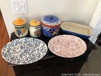 Front view of all six items on a dark surface, showing colorful terracotta and ceramic kitchenware, including jars, serving platters, and baking pan.