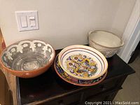 Four terracotta and earthenware serving bowls and dishes on black cabinet, showing natural and colorful patterns