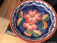 Top view of a terracotta serving bowl with floral painted interior featuring a large red flower with green leaves on a blue background.