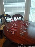 Full view of the set of drink glasses on round wooden table, various types of glasses with red swirls visible