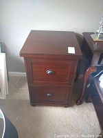 Front angle view of the wood filing cabinet showing two drawers with metal cup pull handles and scratches on top surface.