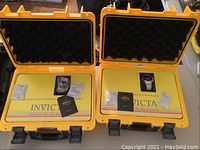 Two open yellow protective cases side by side displaying each watch in foam with booklets and silica gel packets.