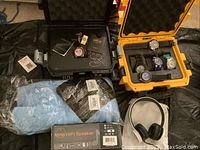 Overview of black and yellow watch cases with six watches, boxed speaker, cleaning cloths and headphones