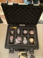 Open black foam-padded hard plastic case with eight Invicta watches arranged in two rows of four