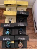 Overhead view of eight watches in two yellow-lined and six black Invicta boxes on wood floor
