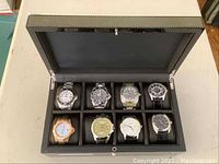Eight watches arranged in black enamel storage box