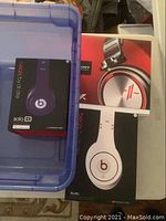 Three boxed headphone sets in blue plastic bin: purple Solo HD, white Studio, Sony box