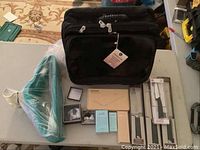 Full overview photo of the lot showing black Joy Mangano bag, teal velvet hangers, boxed fragrances, cutlery in packaging, and small boxes with costume jewelry.
