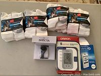 Overview of the items showing four packs of white Hanes socks, Invicta Snoopy watch in box, Omron 5 Series blood pressure monitor, and OneTouch Verio IQ glucose monitor