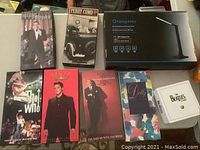 Eight items arranged on a flat surface: seven CD box sets and one boxed LED desk lamp