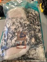 Rug in clear sealed plastic packaging showing brand label and mottled black and white wool pattern.