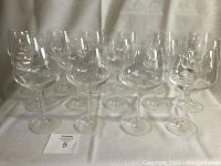 Fifteen large clear red wine glasses arranged standing in rows on a white fabric surface.