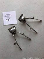 Two vintage handheld manual hair clippers displayed on a gray surface, showing full front and side views clearly.