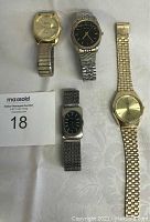 Four men’s wristwatches arranged on fabric background with auction tag.