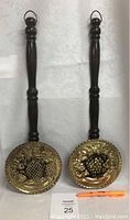 Front view of two wooden handled decorative brass bed warmers featuring fruit motif embossing.