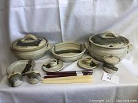 Front view of entire handmade pottery set including covered pots, serving dish, salt and pepper shakers, sugar bowl, plate, bowl, candle holders with candles, and chopsticks.