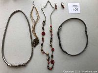 Full view of jewelry and belts laid on white surface showing three necklaces, one pair of earrings, and two belts.