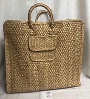 Front view of large hand woven bag showing flap pocket and two round handles