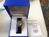 Tommy Star women's watch displayed inside its original box with beige interior and blue exterior, watch features black leather strap and silver-tone case.