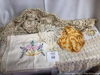 Wide view showing embroidered pillowcase with basket of flowers, two crocheted doilies and lace linens beneath