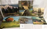 Six vintage fine art prints showing landscapes and a portrait arranged on a surface