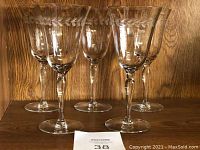 Five vintage etched wine glasses displayed on a wooden surface, showing their clear glass construction and faceted stems.