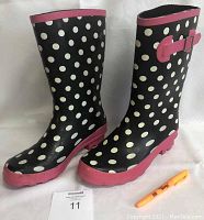 Pair of women's rain boots size 9 with black and white polka dot pattern, pink soles and trim, shown from side and front angles with a size tag and highlighter for scale