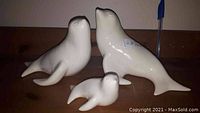 Front view of three ceramic sea lion figurines of varying sizes on a wooden surface under warm light.