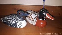 Side view of two hand-carved and hand-painted wooden ducks on a brown wooden surface.