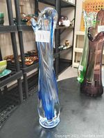 Clear glass vase with blue swirling pattern and flared top, displayed on a shelf among other glassware items.