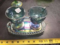 Front view of blue iridescent glass sugar bowl and creamer set on matching tray with measuring tape for size reference.
