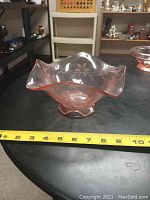Side angle view showing scalloped edge and floral pattern on pink glass bowl with measuring tape showing about 8 inches width.
