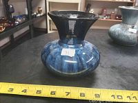 Front angle showing vase shape, blue marbled glaze and flared neck with measuring tape indicating size.