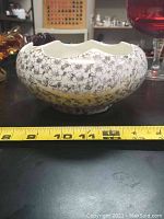 Side profile of scalloped edge vintage pottery bowl with black floral pattern on cream pottery. Measuring tape shows approximately 7 inches width.