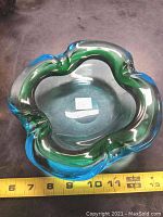Top view of the chalets glass ashtray showing the green and blue thick glass with wavy rim and a measuring tape showing around 5 inches wide.
