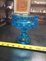 Full side view of vintage blue chalice-type glass compote with measuring tape showing approximately 7 inches width and 6 inches height.