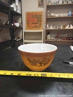 Front view of the bowl showing the fruit design on the yellow exterior with a measuring tape for scale (approx. 5.75 inches wide).