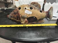 Side view of glazed ceramic fish figurine showing hole pattern and colors with measuring tape indicating about 13 inches length.