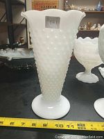 Front side view of 9.5 inch tall white hobnail milk glass vase with flared ruffled rim and pedestal base against black background.