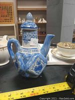 Blue and white teapot showing the front with floral and geometric pattern with hexagonal body shape.