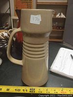 Side view showing the tall ceramic pitcher with handle and horizontal ridges around the middle. Yellow measuring tape confirming height at 10 inches.
