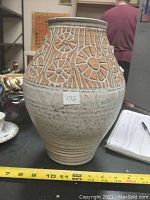 Side view of the beige ceramic vase with raised terracotta floral and geometric pattern, showing size about 10 inches tall.