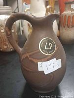 Front view showing the brown ceramic pitcher with decorative tan glaze streaks and maker's mark sticker reading LP Burenjanje handcrafted in Canada with price tag.