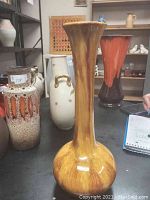 Full side view of tall brown glazed ceramic vase with flared opening.