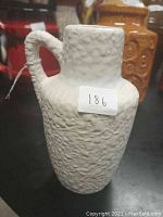 Image showing front and side view of textured white ceramic pitcher with handle and sticker labeled '186'.