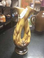 Photo shows front view of the unique double-spout vase with yellow and brown glaze on black surface.