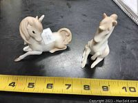 Two vintage miniature unicorn figurines side by side shown from above with a yellow measuring tape showing length between 4 and 5 inches.