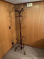 Full view of bent wood coat rack standing in corner of room, showing complete structure and multiple curved hooks at top and base.