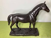 Side view of the cast metal horse sculpture showing full body and base, against a light green surface and white background.